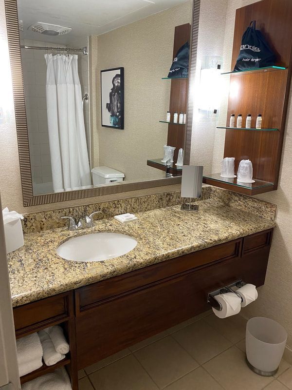 Bathroom with granite countertop, large mirror, and wooden vanity. Includes a shower, toiletries, and towels.