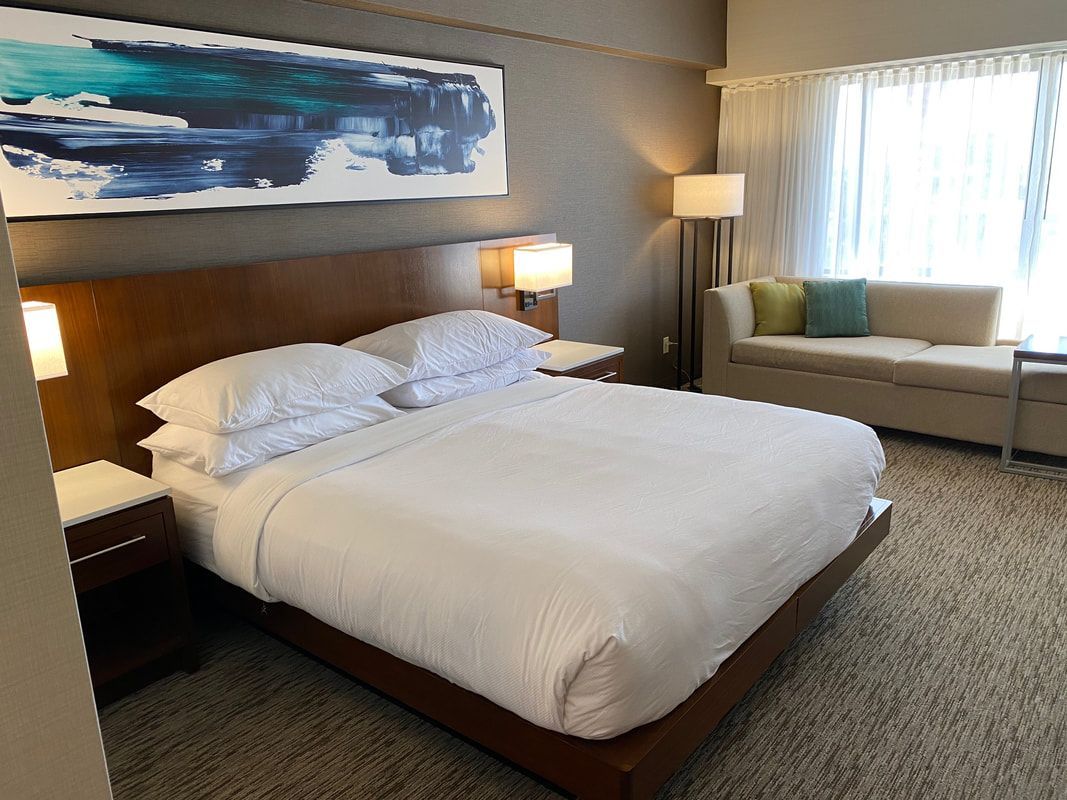 Hotel bedroom with a bed, artwork, and a sofa.