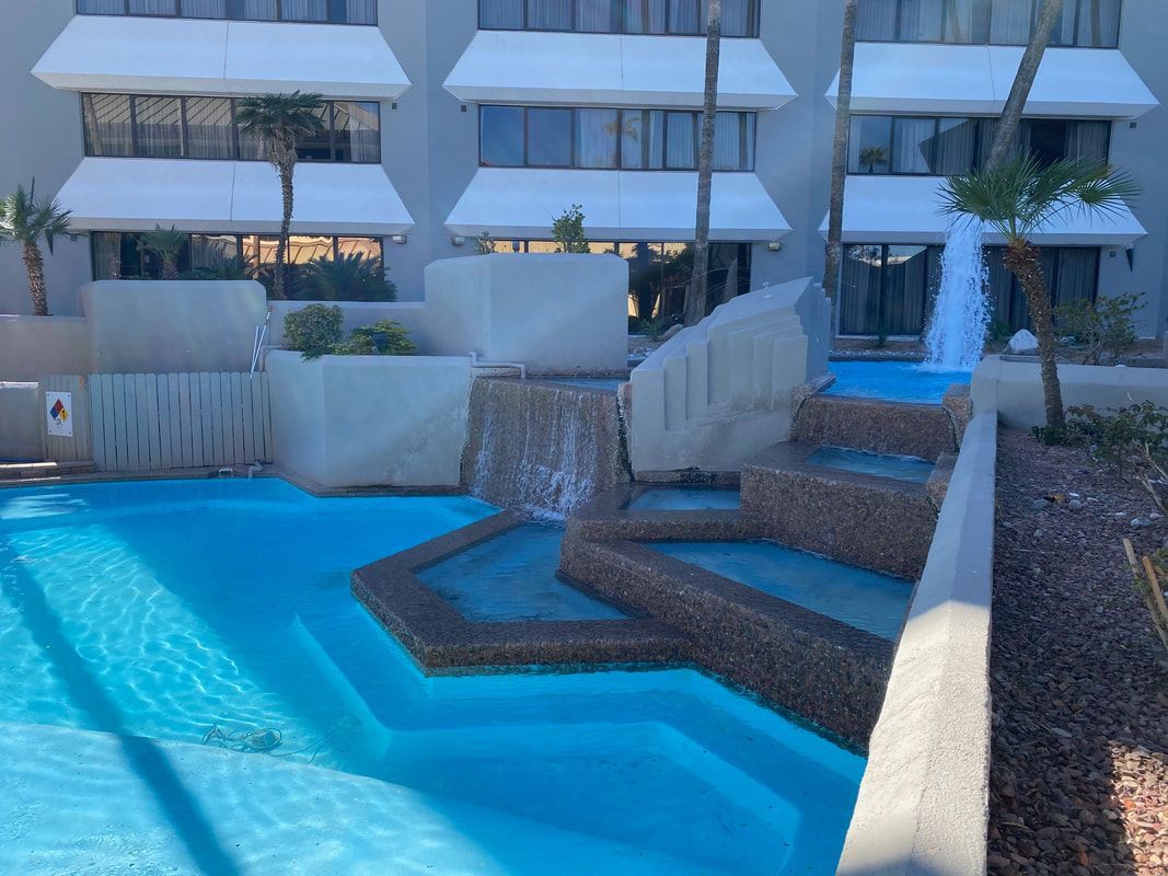 Pool with a tiered waterfall feature in front of a multi-story building with white trim.
