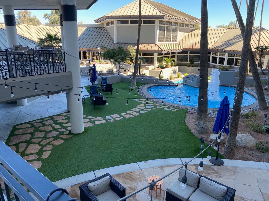Outdoor patio with fountain, seating, and building in the background; green lawn and stone pathways.