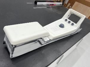 White prototype device with screen, buttons, and hand rest on a black surface.