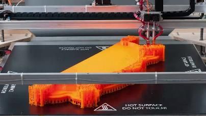 3D printer in action, depositing orange plastic onto a black surface. Supports surround the part being printed.