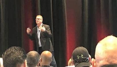 A man is standing on a stage giving a presentation to a group of people.