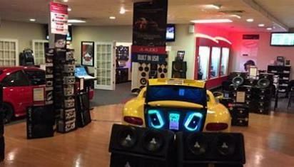 A yellow car is sitting in a room surrounded by speakers.
