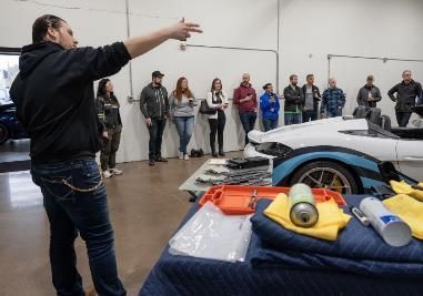 A man is giving a presentation to a group of people in a garage.