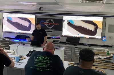 A group of men are sitting in front of a projector screen in a classroom.
