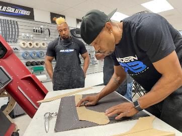 Two men are working on a piece of leather on a table.