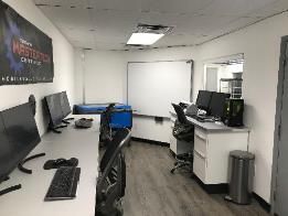 A room filled with desks , chairs , computers and a whiteboard.