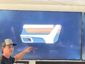 Man pointing at a car door design on a screen. The design is white, blue and wood-tone.