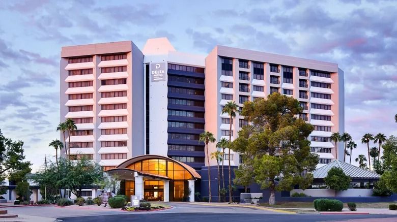 Hotel exterior with palm trees, light and dark tan/gray building with arched entrance and glass doors.