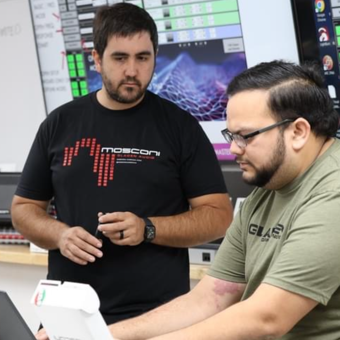 Two men wearing moscon shirts are looking at a laptop
