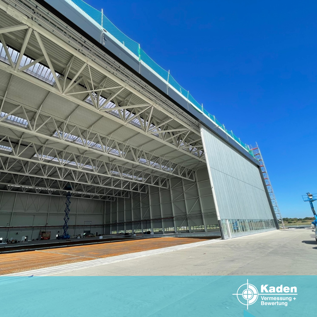 Großer, offener Industriehangar mit weißem Metallgerüst vor blauem Himmel.