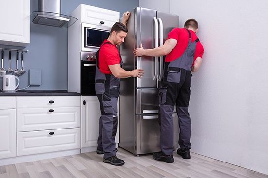 Male Movers Placing Steel Refrigerator in Kitchen — Cape Cod, MA — Cape Appliance Repairs