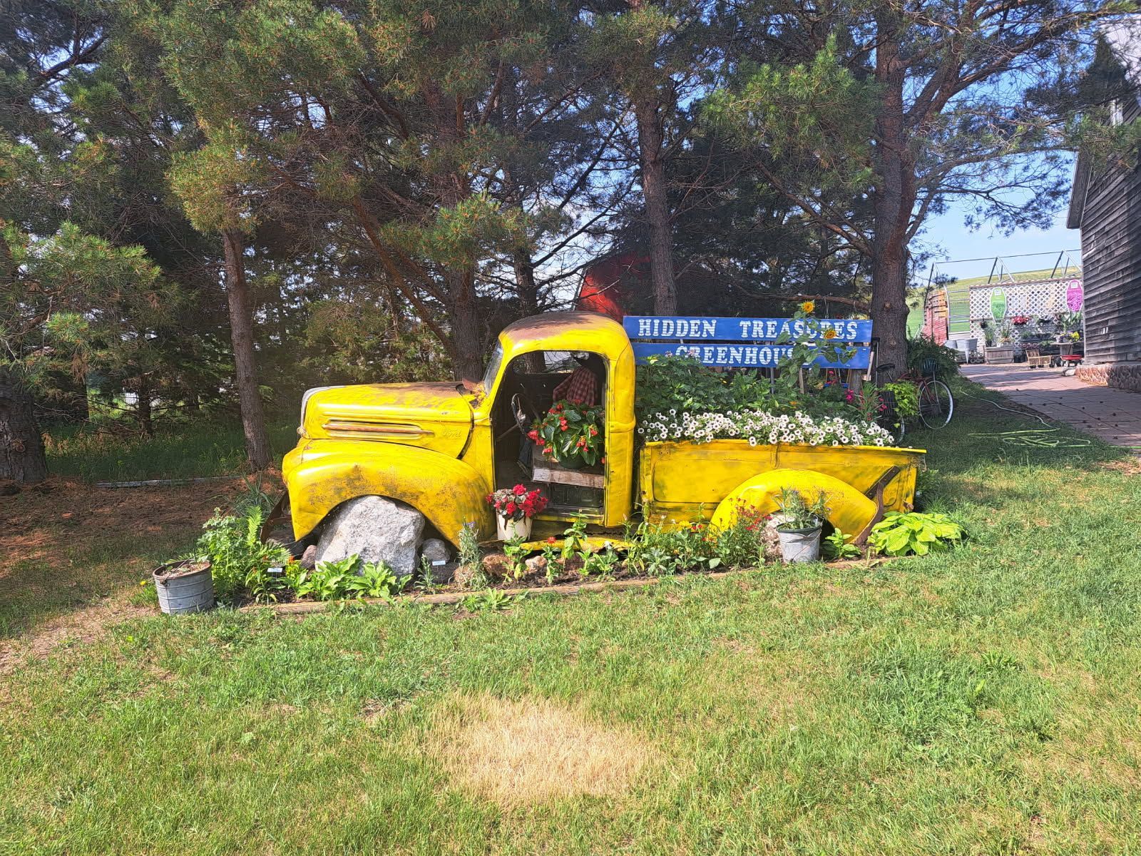 Yellow vintage truck filled with flowers, used as a garden decoration at Hidden Treasures Greenhouse.