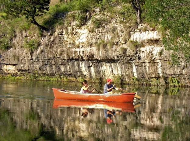 A man and a woman are paddling a red canoe on a lake.
