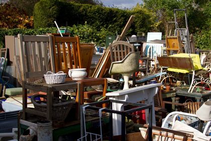 Pile of old furniture and objects outdoors, including chairs, tables, and a birdbath.