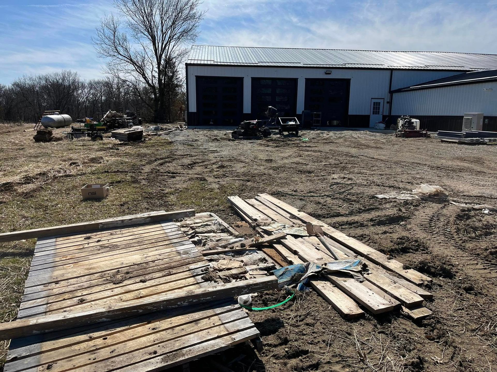 Construction site with wooden pallets, equipment, and a large building with garage doors.