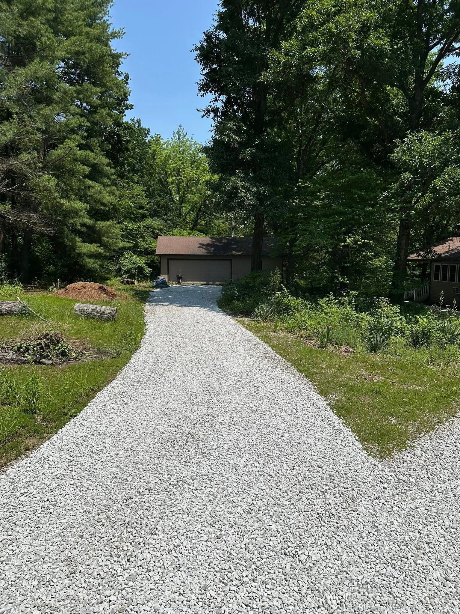 Gravel pathway leading toward a building with a brown roof, flanked by greenery and trees under a clear sky.