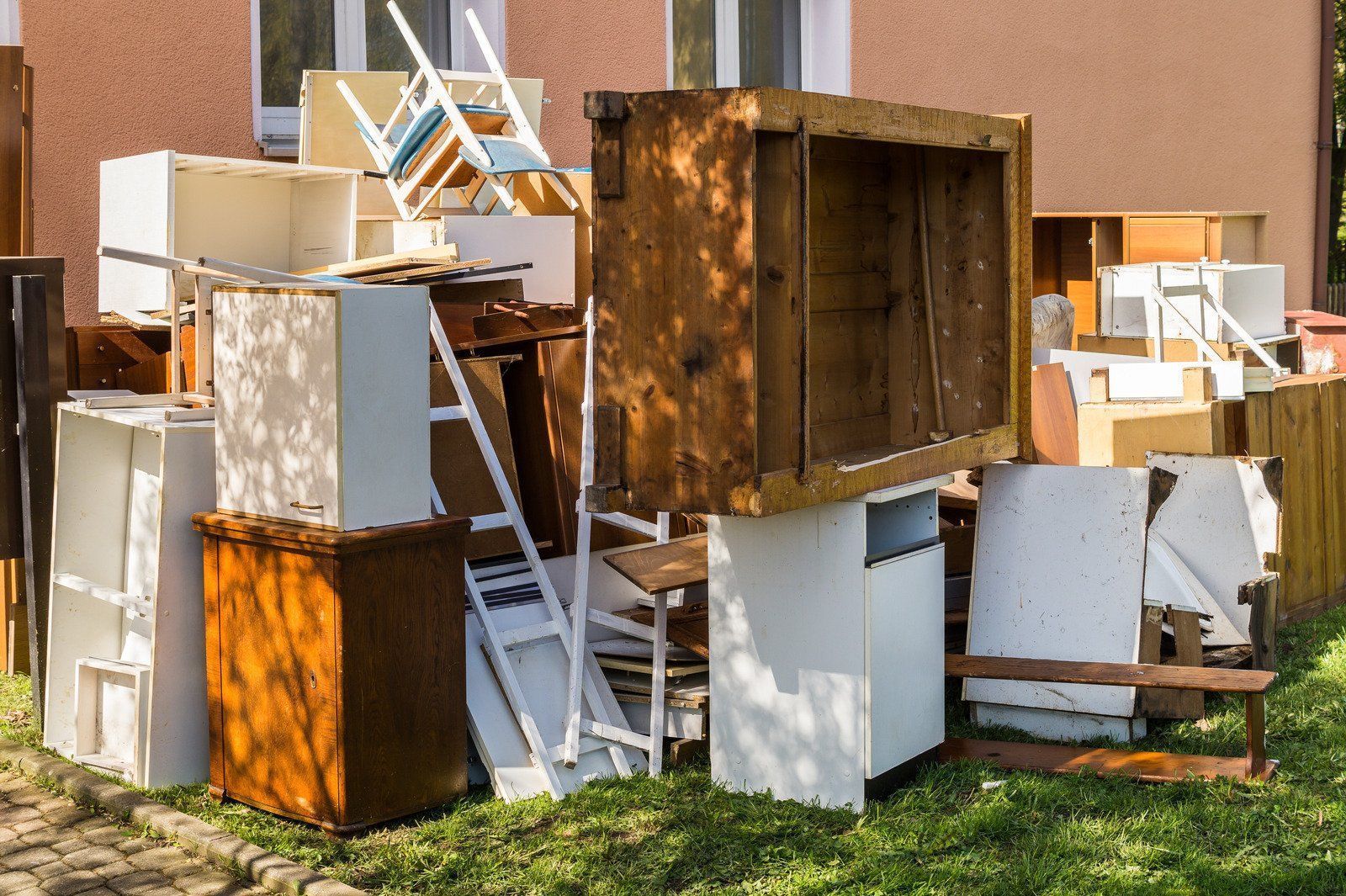 Pile of discarded cabinets and furniture on grass next to a building.