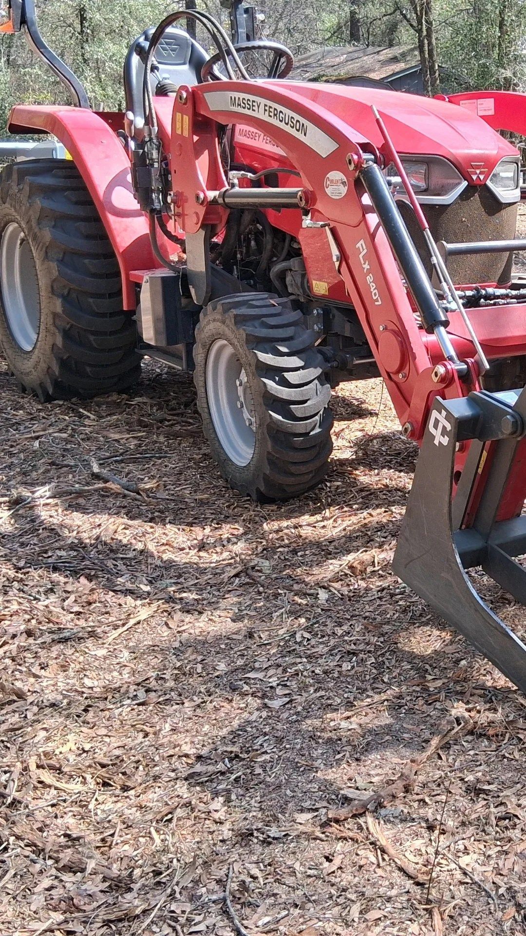 Red tractor with a front loader parked on a leaf-covered wooded trail