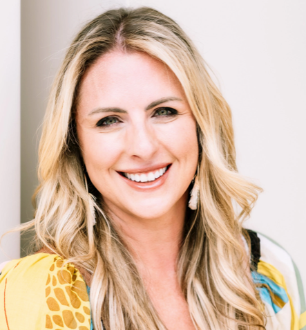 Woman with blonde hair smiling, wearing a colorful patterned top.