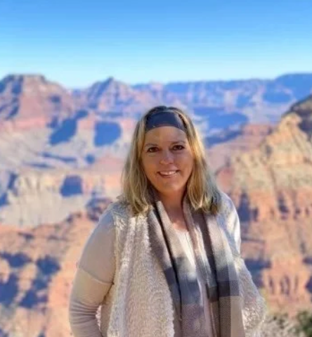 Woman in cream-colored clothing and scarf smiles, posing in front of the Grand Canyon.