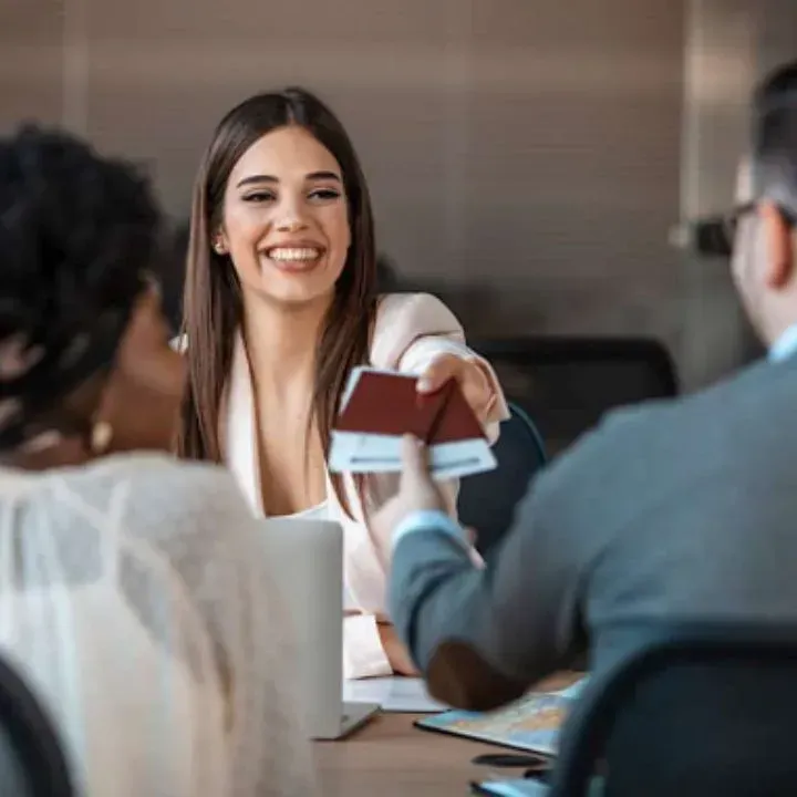 Woman smiling, handing passports to a person at a desk in an office setting.