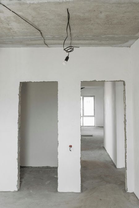Interior view of a room under construction, featuring doorways, unfinished walls, and exposed wiring; gray and white tones.