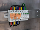 Electrical surge protection device mounted on a rail, featuring orange fuse holders, multicolored wires, and a green ground.
