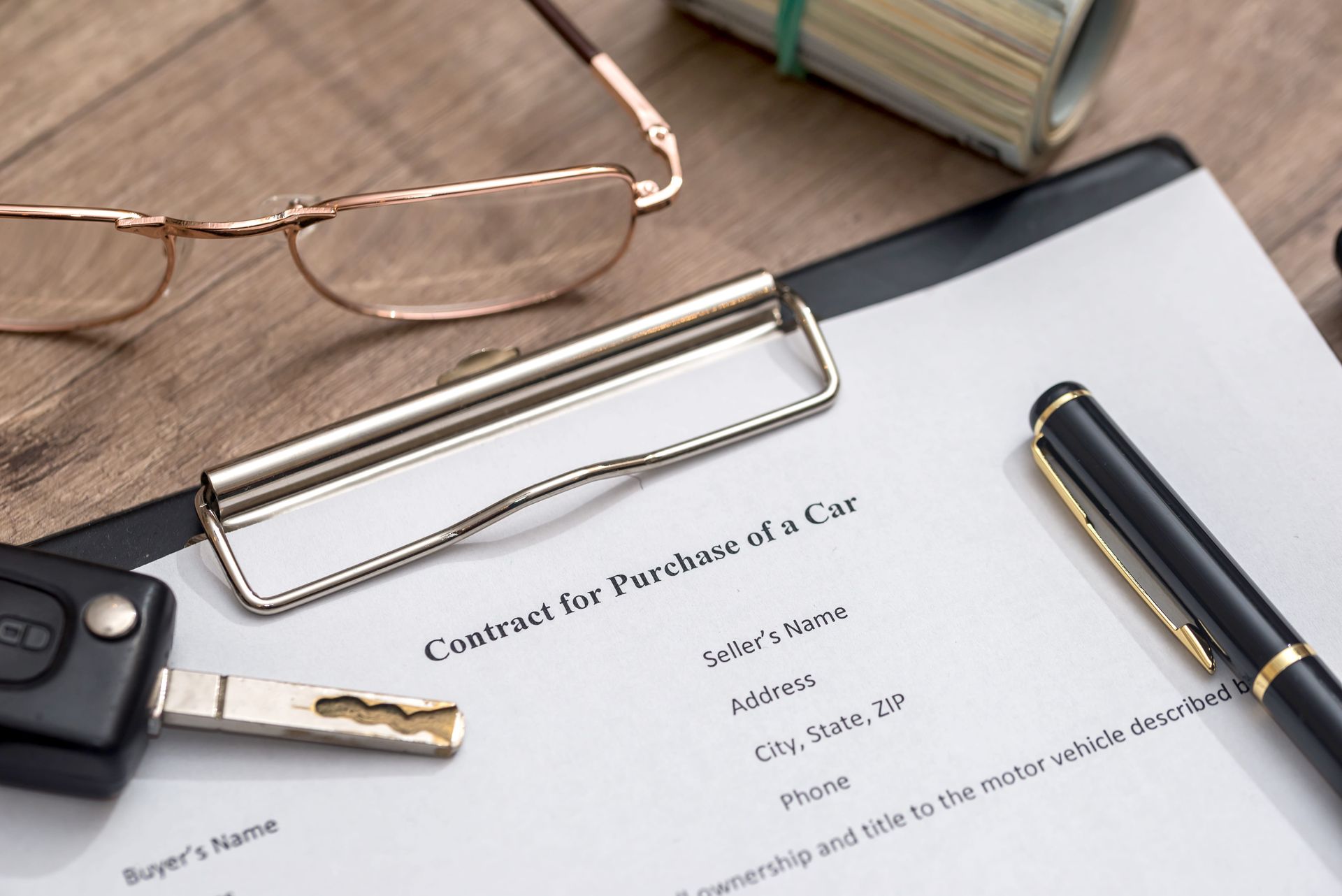 Desk with clipboard, eyeglasses, car key, pen, and a contact form on paper.