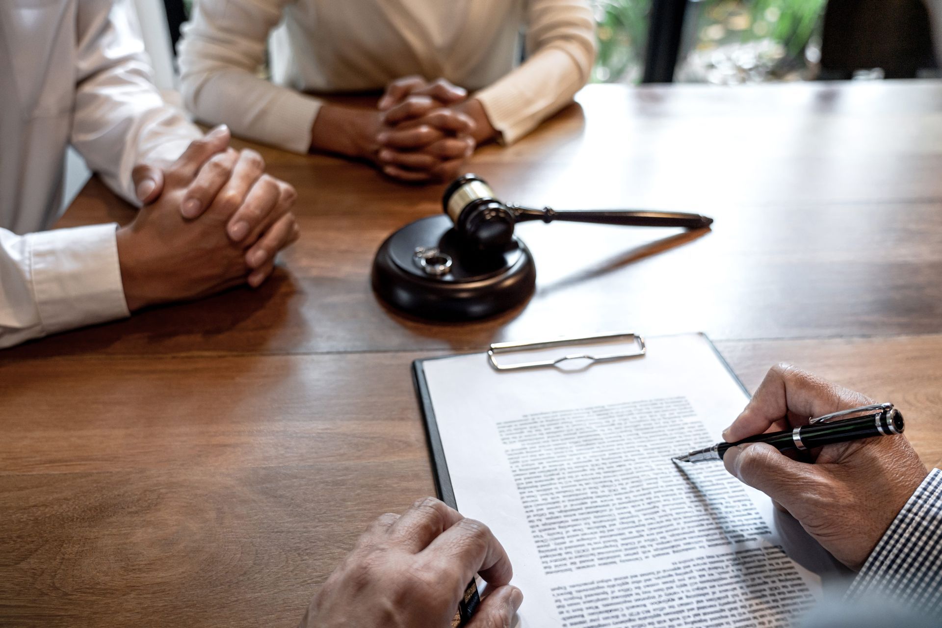 People signing legal documents at a wooden table with a judge’s gavel and clipboard