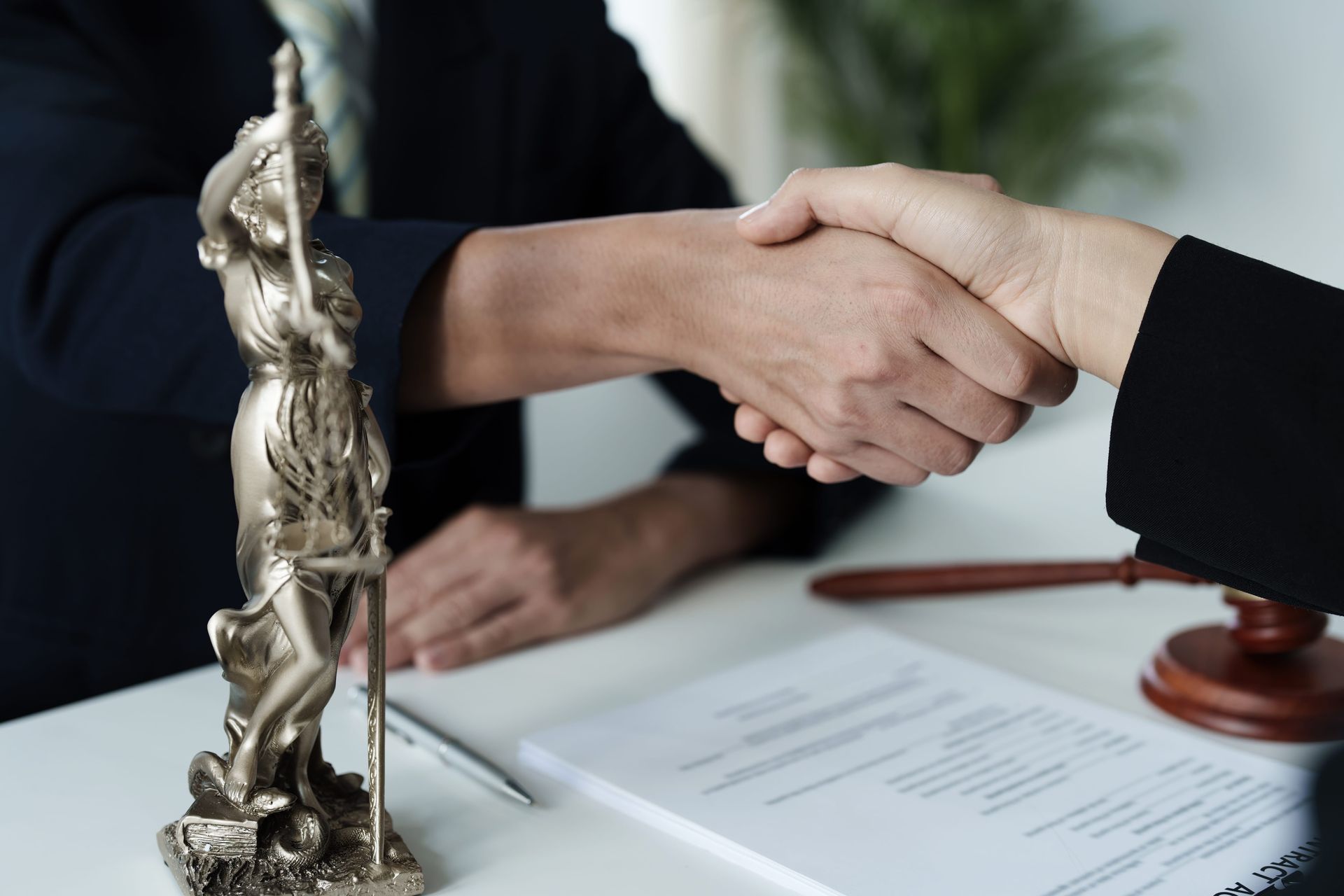 Handshake over a legal contract with a judge’s gavel and scales on a desk