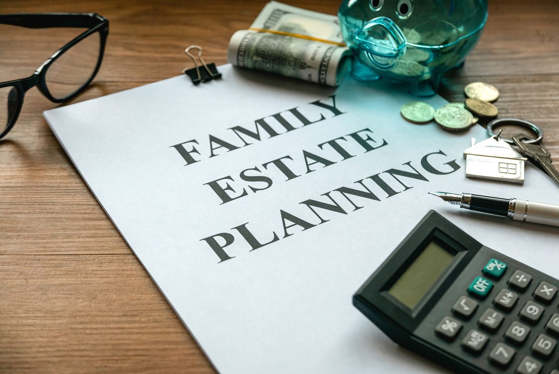 Family estate planning documents on a desk with calculator, eyeglasses, keys, and a piggy bank.