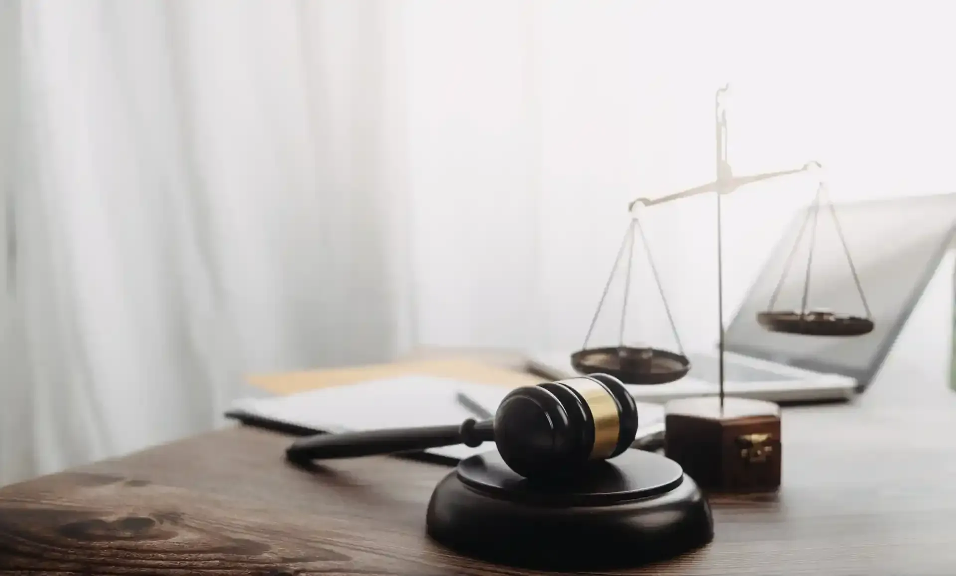 Gavel and scales of justice on a desk with a laptop and papers, representing legal proceedings.