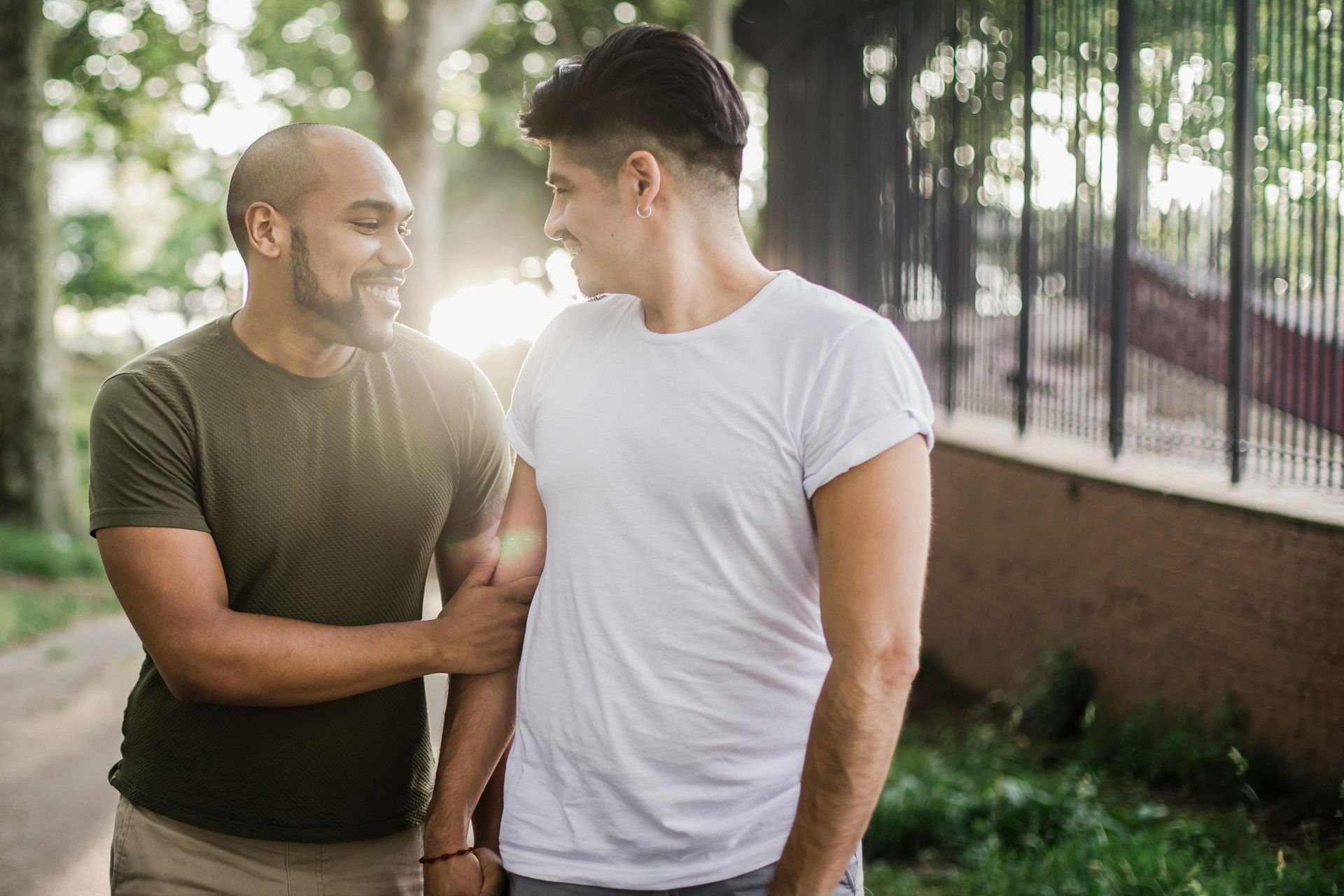 Two people look at each other and smile while walking together outdoors in the soft sunlight.