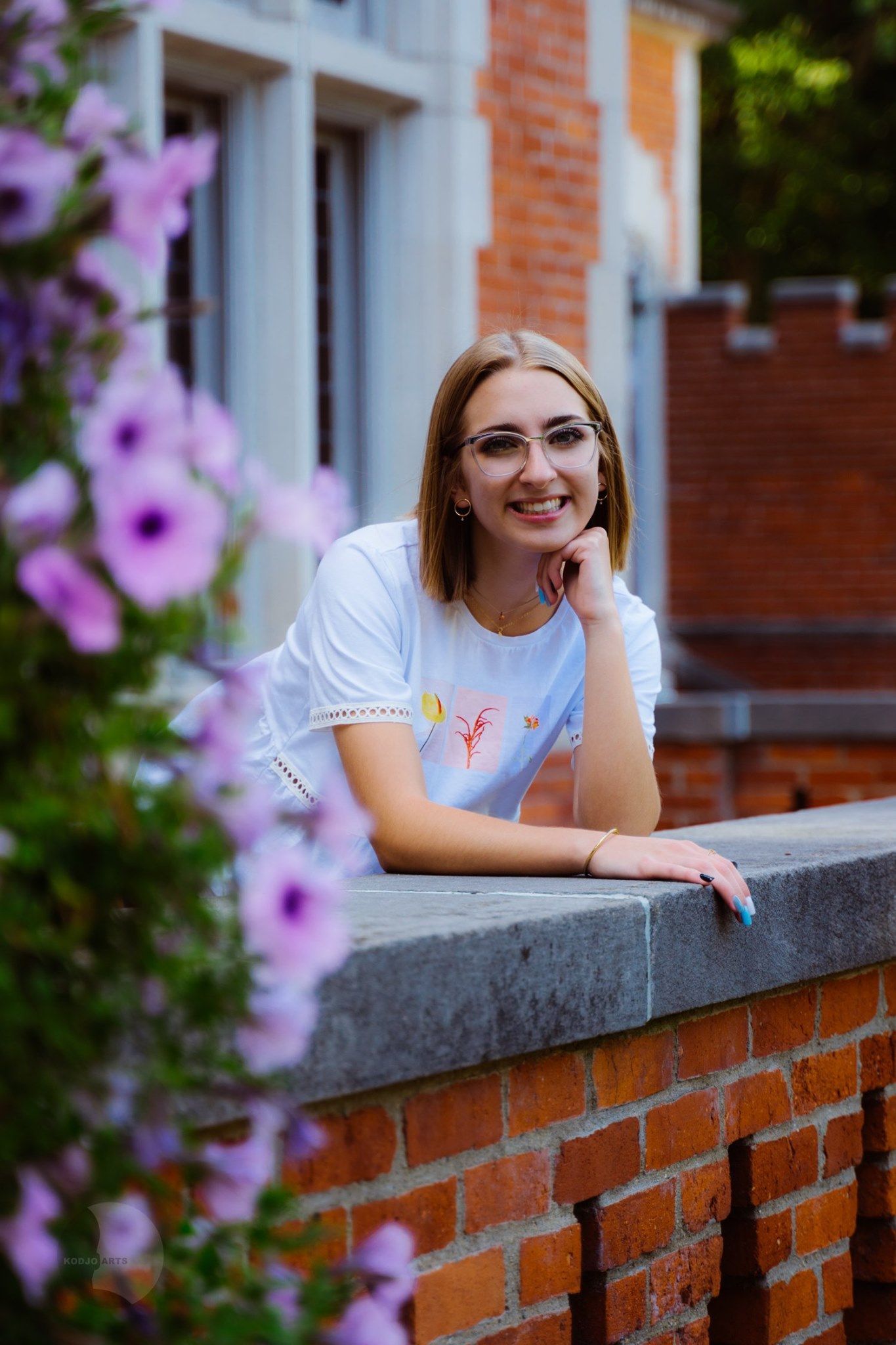 Senior eaning on a brick wall with purple flowers in the background.