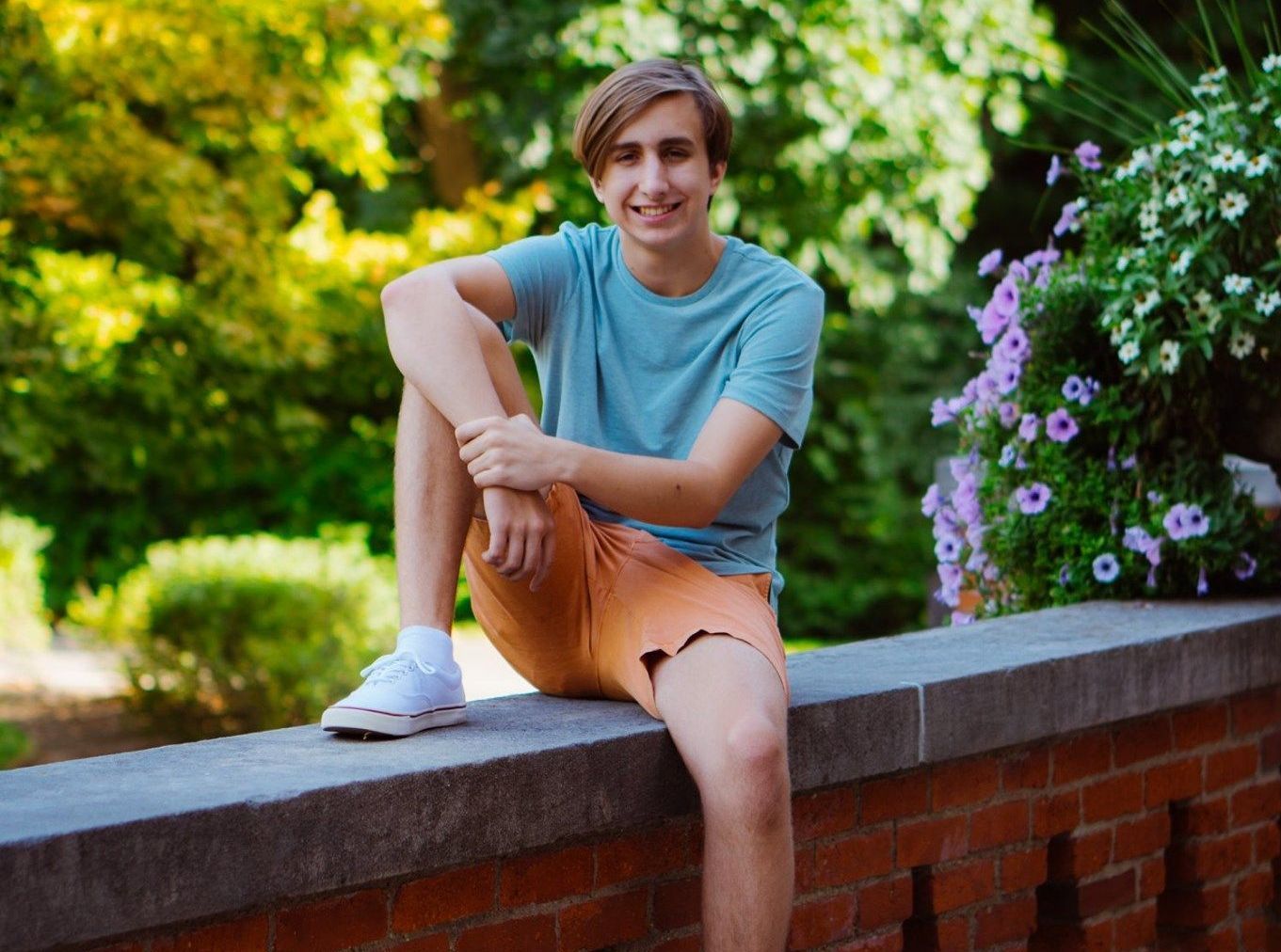 A high school senior is sitting on a brick wall .