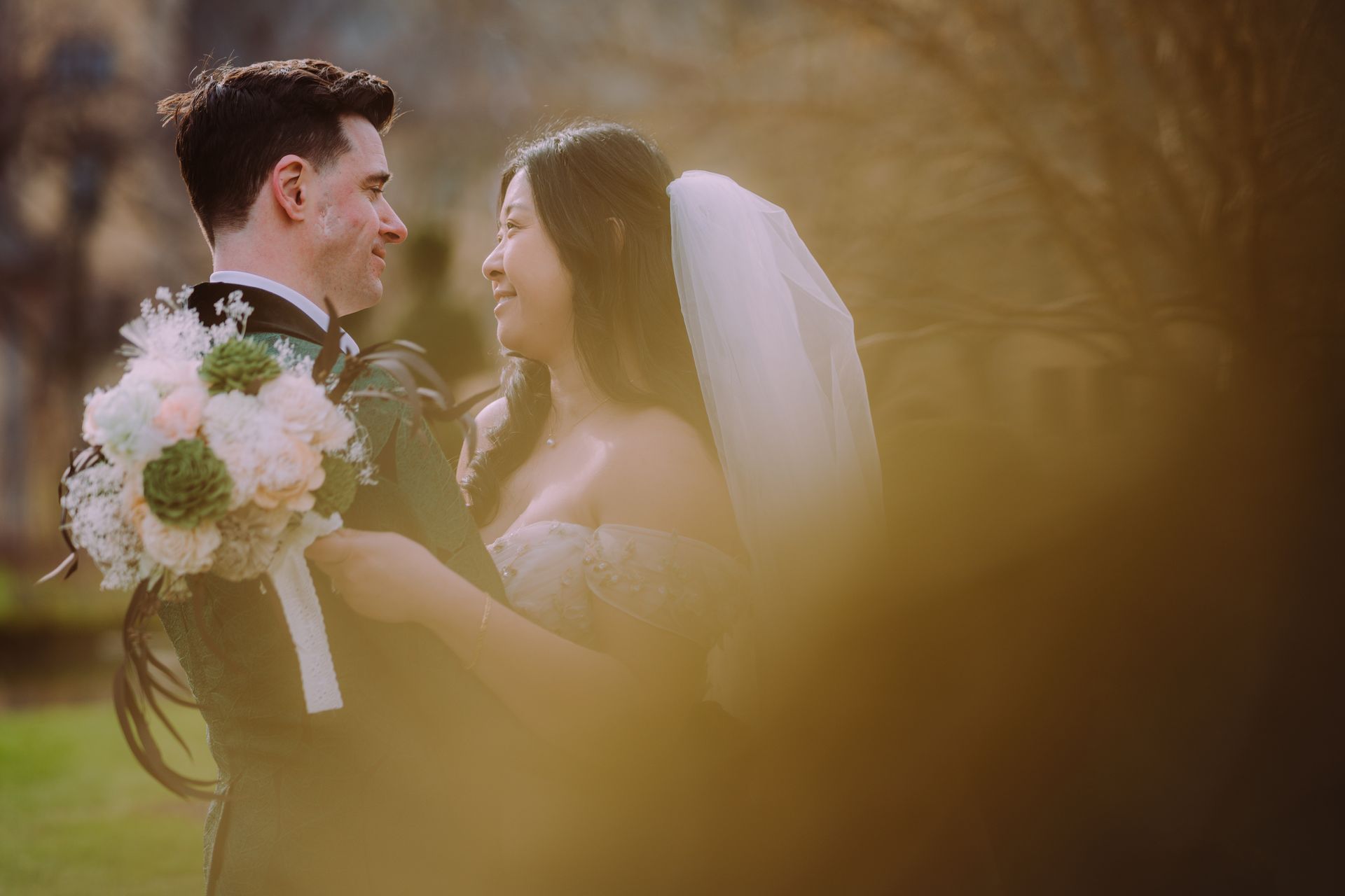 Bride and groom smiling with bouquet in a warm outdoor wedding scene