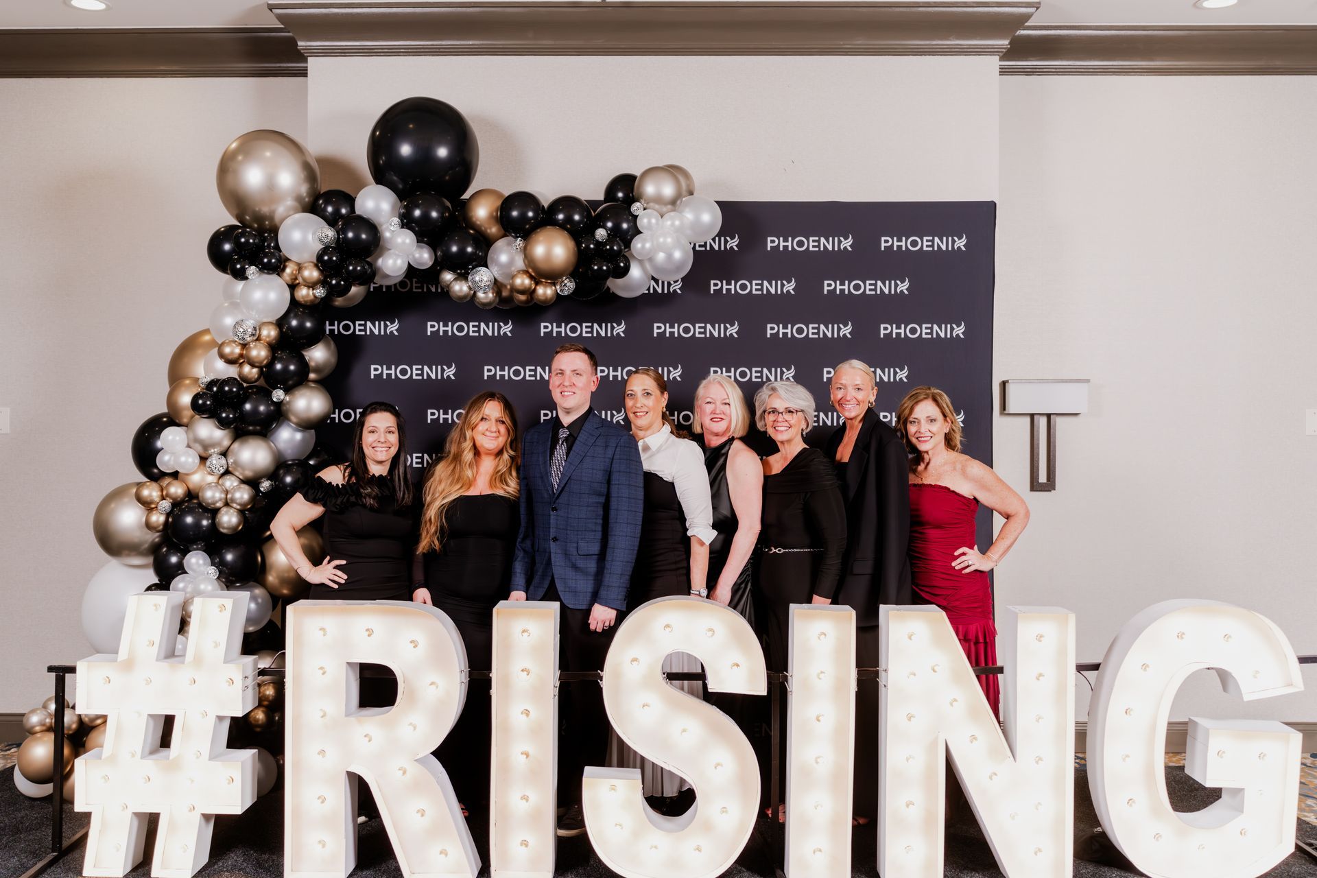 A group of eight people stand in front of a Phoenix-branded backdrop and giant illuminated letters spelling 