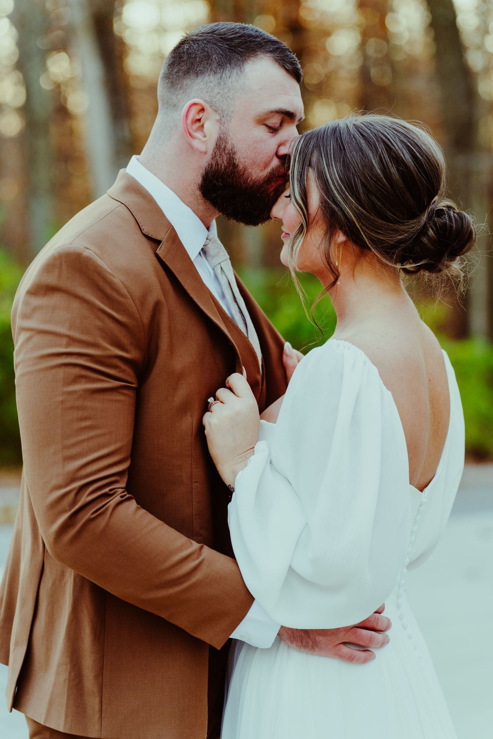 a bride and groom are kissing in front of a wooded area.