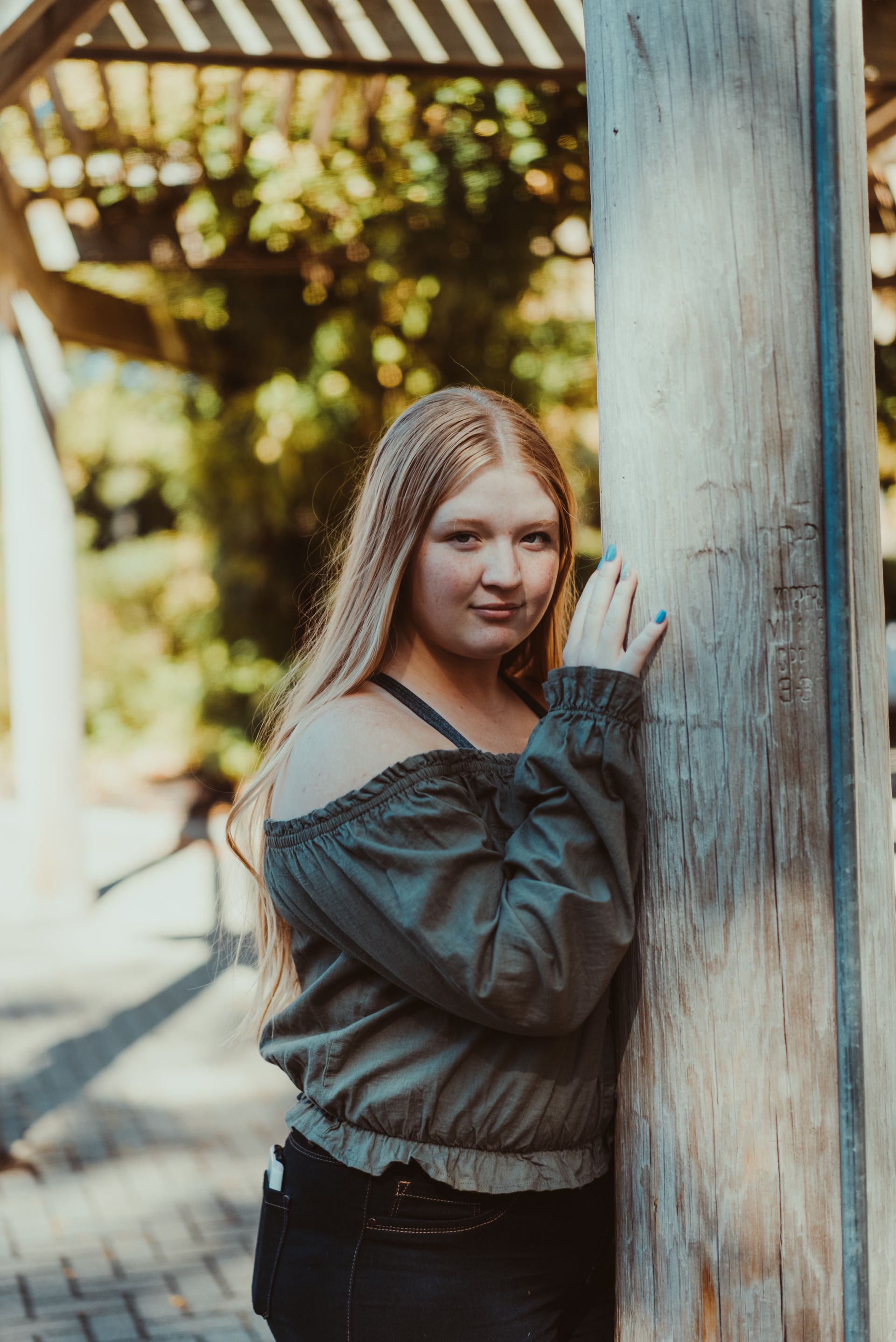 A young woman is leaning against a wooden pole.