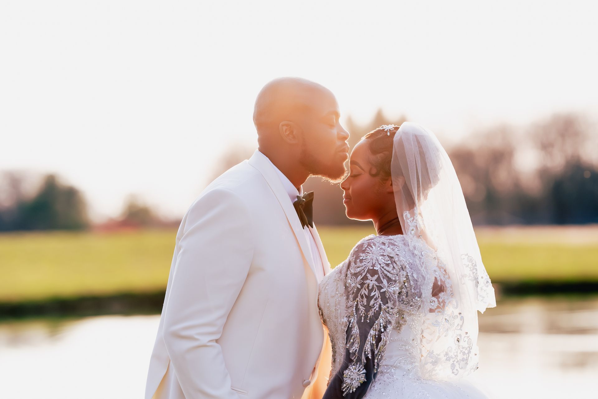 A bride and groom are kissing in front of a lake.