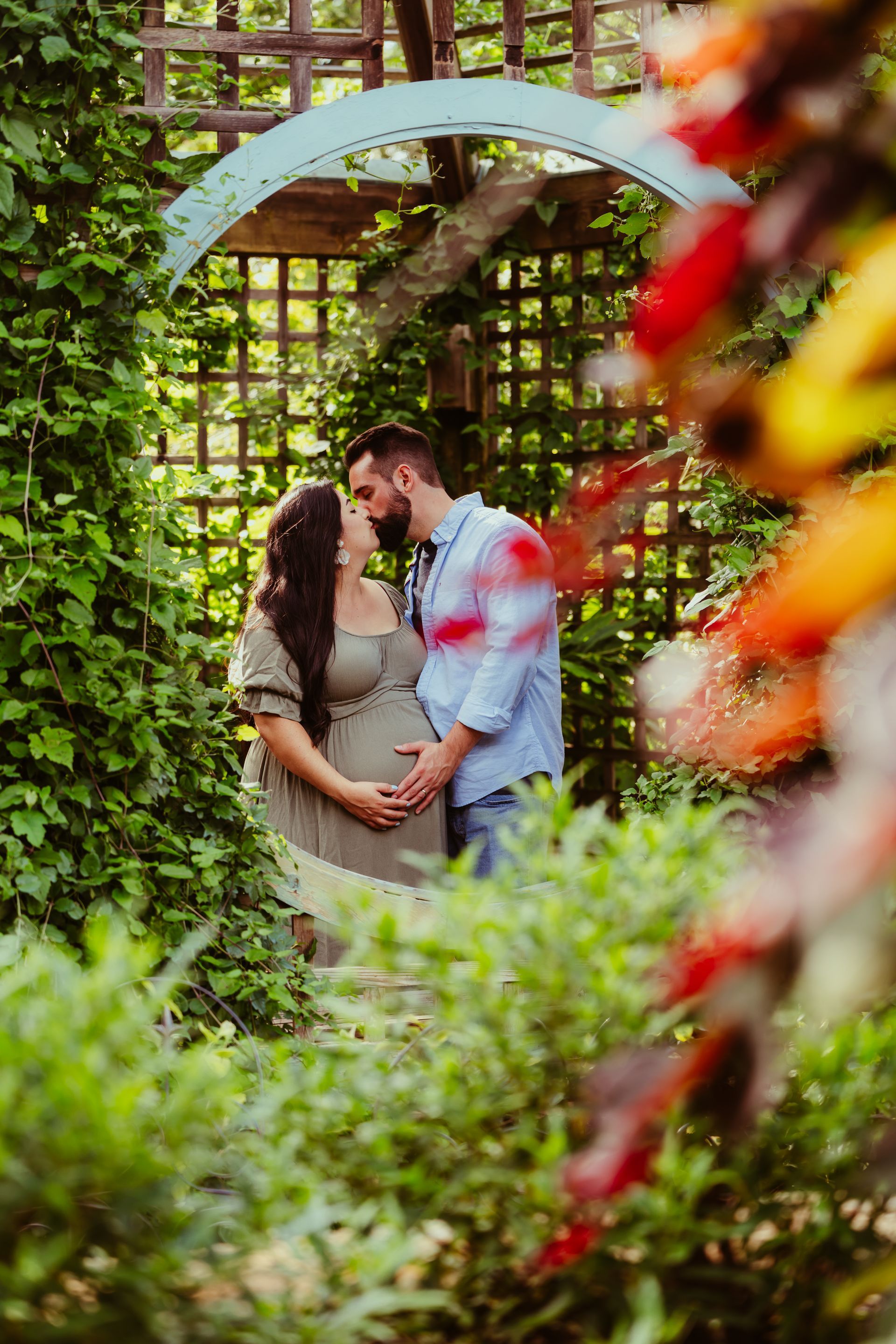 a pregnant woman and a man are kissing in a garden .