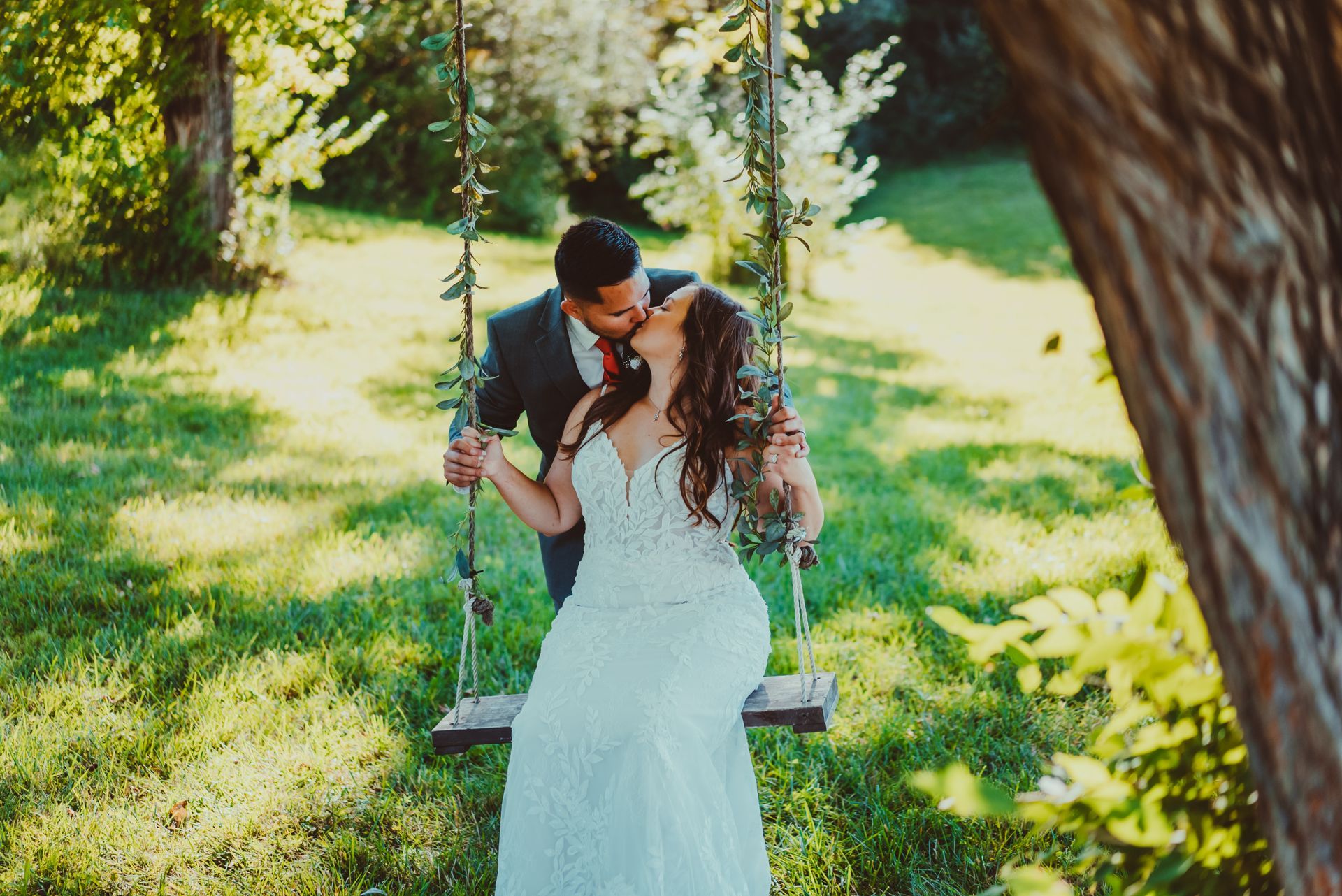 a bride and groom are kissing while sitting on a swing .