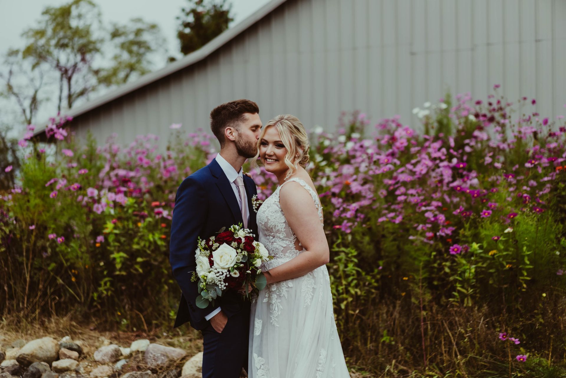 a bride and groom are kissing in front of a field of pink flowers .
