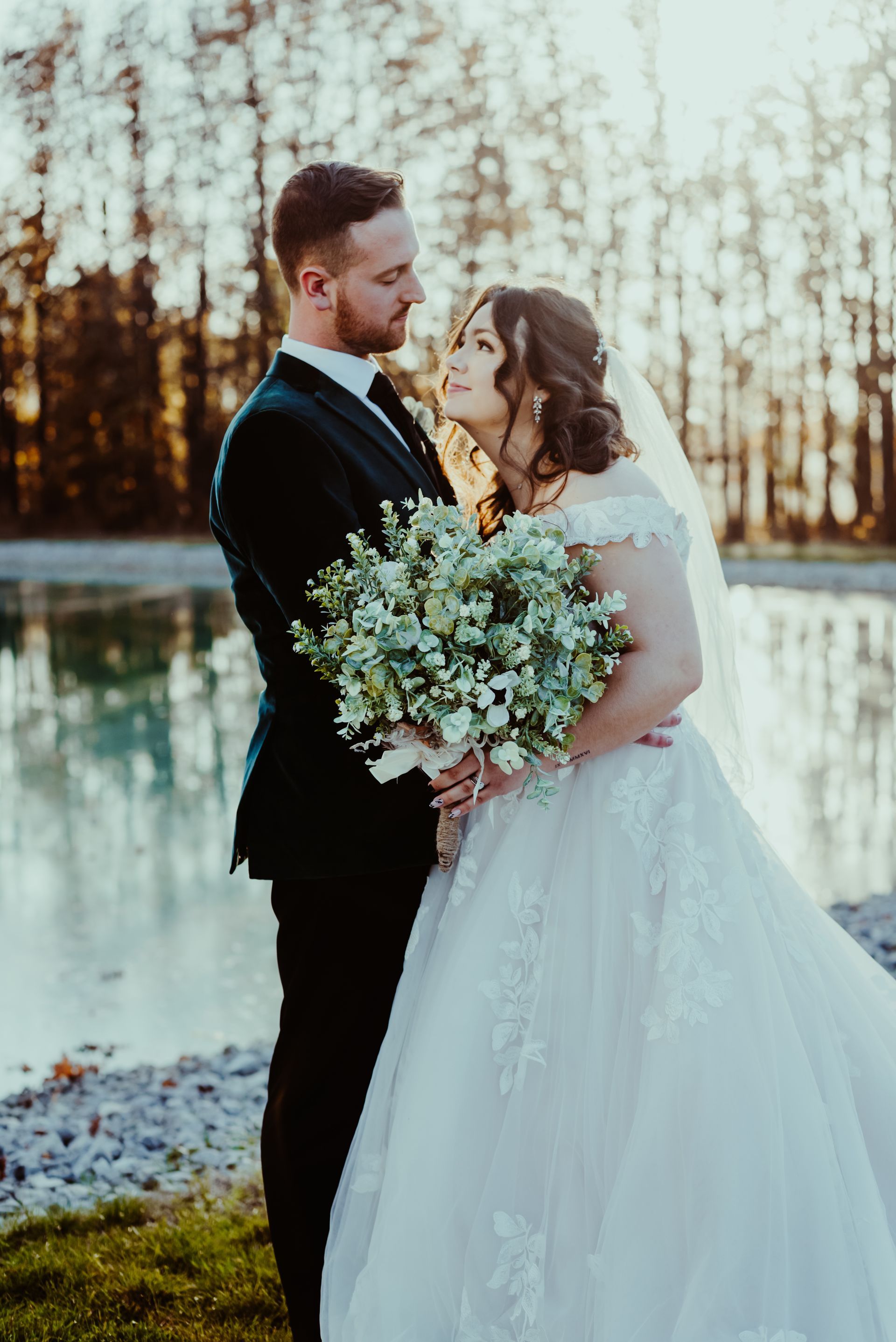 a bride and groom are posing for a picture in front of a lake .