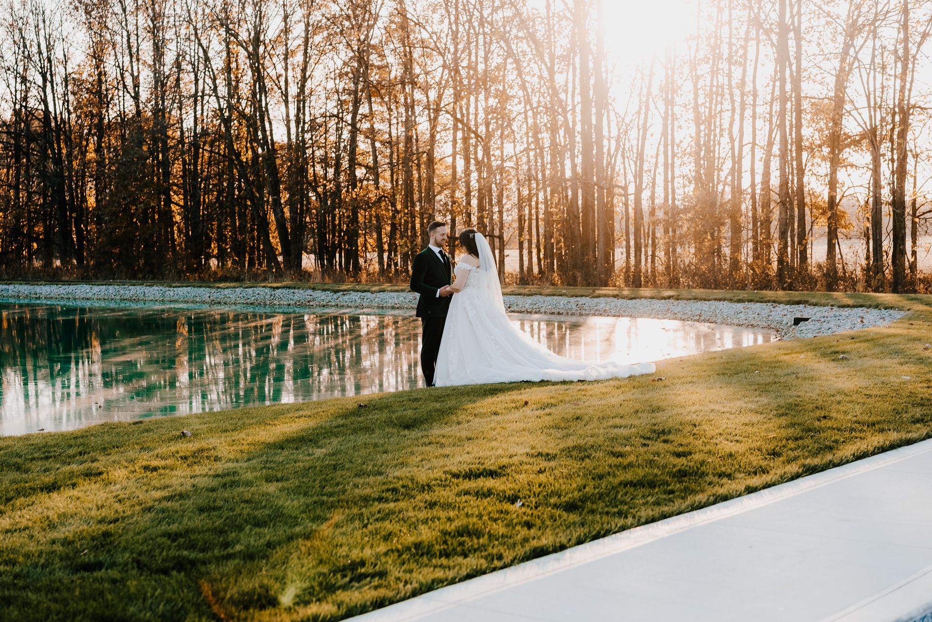 a bride and groom are standing next to a pond .