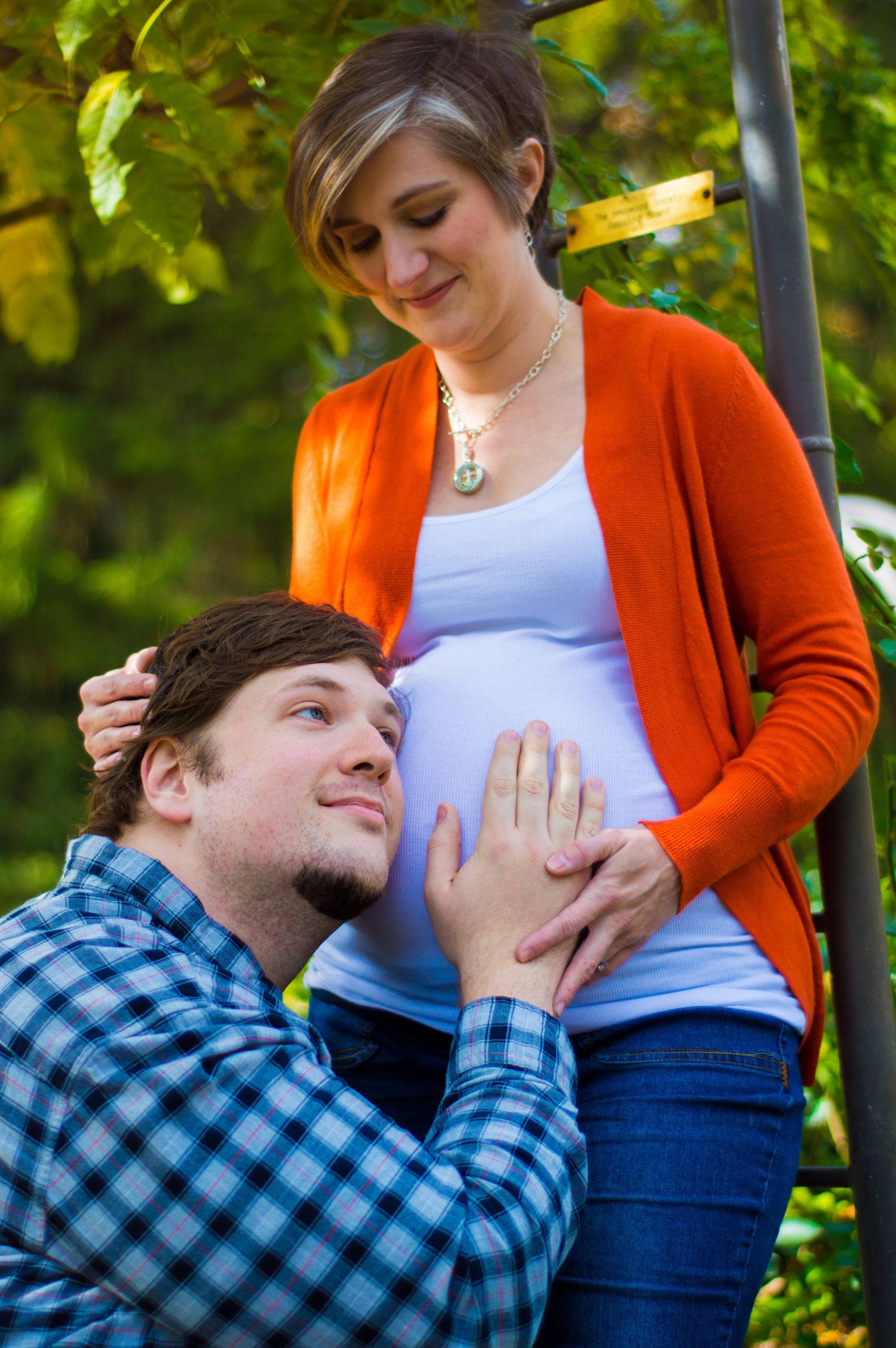 a man is kissing a pregnant woman 's belly in a park .