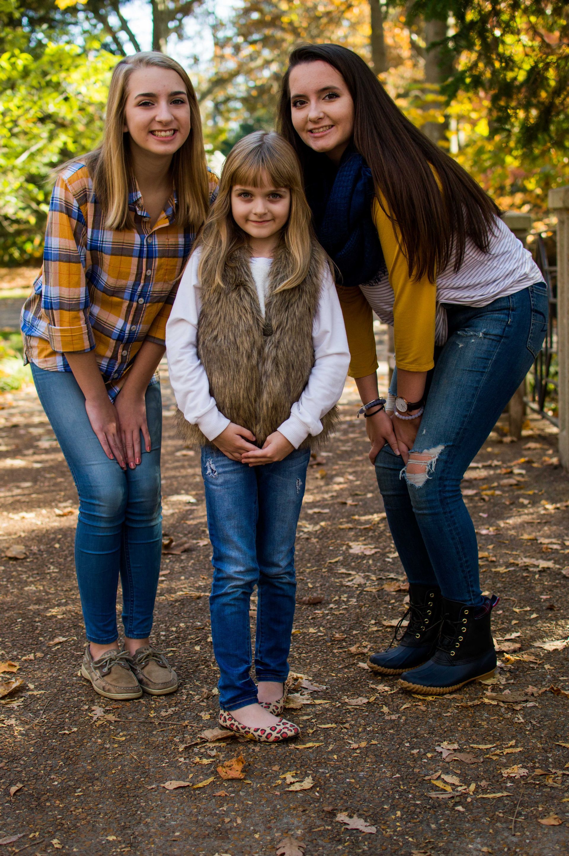 three girls are posing for a picture in a park .