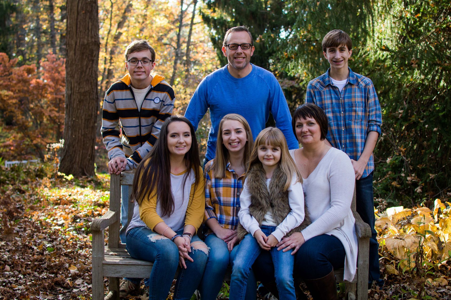 a family is posing for a picture while sitting on a bench in the woods .